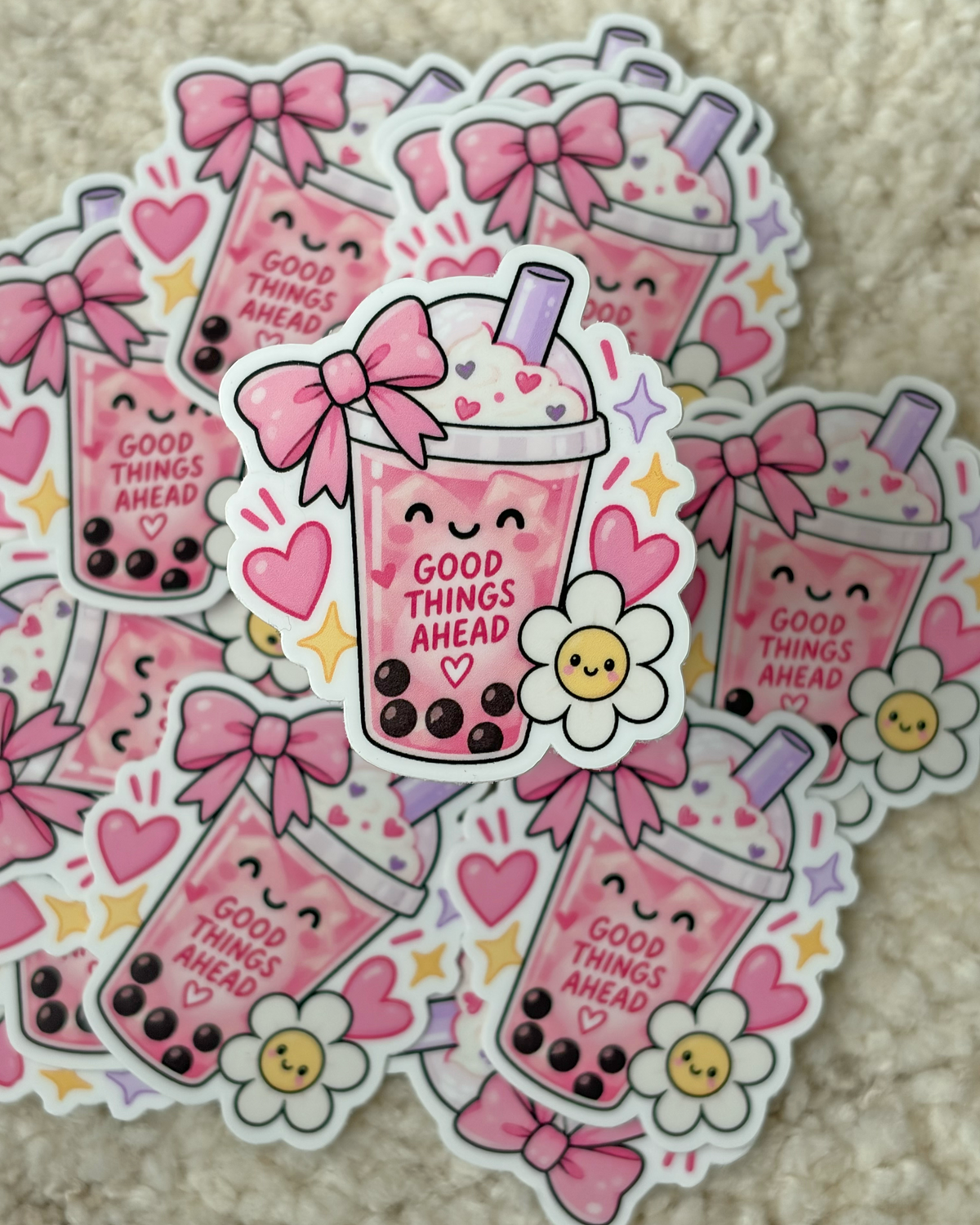 A pile of die-cut stickers featuring a cute pink boba drink character with the text 'GOOD THINGS AHEAD' on a beige textured background.
