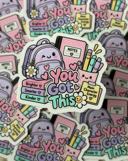 A close-up of a die-cut sticker featuring a cute pastel illustration with the phrase 'You Got This' in colorful bubble letters, surrounded by school-themed icons like books, pencils, a flower, and a smiling backpack. Multiple identical stickers are scattered in the background.