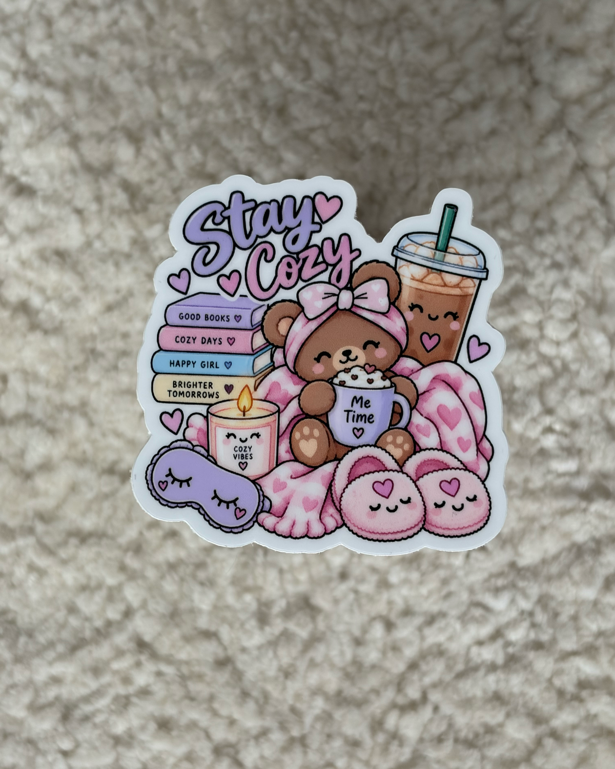 A die-cut sticker featuring a cute cartoon teddy bear wrapped in a pink blanket with a pink drink, candles, and a sleep mask, alongside the text 'Stay Cute' and 'GOOD MAMAS', placed on a textured beige carpet.