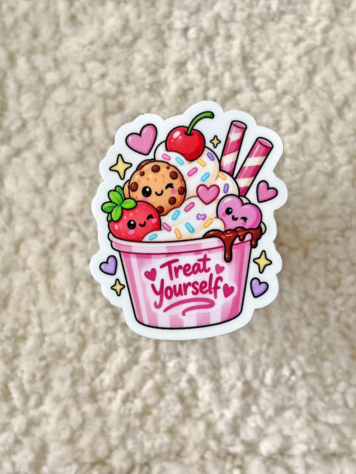 A die-cut sticker featuring a cute cartoon ice cream cup with the words 'Treat Yourself' written on the pink cup, placed on a textured beige fabric background.