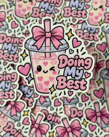 A die-cut sticker featuring a cute pink bubble tea cup with a smiling face, heart details, a pink bow, and the phrase 'Doing My Best' in pink and lavender lettering. The sticker is shown layered over a repeating pile of the same sticker design.