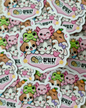A close-up pile of cartoon animal stickers featuring cute dogs, cats, and frogs with hearts and the text 'LUZY DESIGNS' on a pink heart-shaped badge.