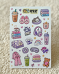 A sheet of cute, cozy planner stickers featuring illustrations of a sleeping cat, pink bunny ears, a cozy drink, books, headphones, pajamas, and a teddy bear, displayed on a textured beige fabric background.
