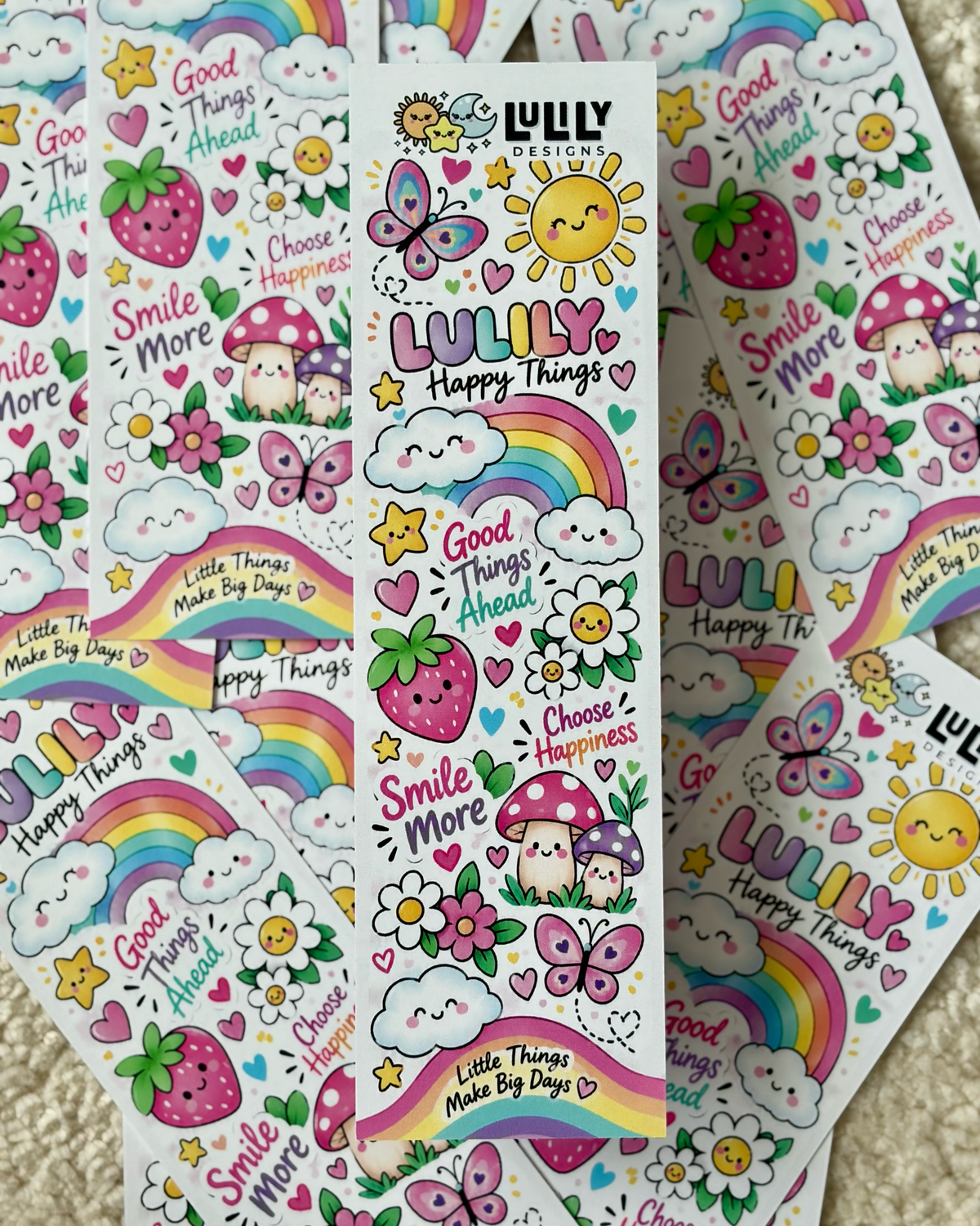 A collection of colorful sticker sheets featuring cute cartoon illustrations including rainbows, butterflies, strawberries, mushrooms, smiling suns, and text like 'LULU Happy Things' and 'Smile More' on a soft beige carpet background.